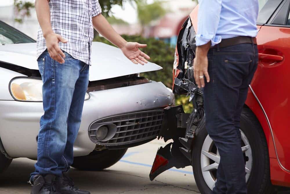 Two men stand near two cars involved in a rear-end collision. The front of a white car and the back of a red car are visibly damaged.