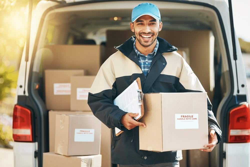 Delivery person holding a box and clipboard, standing in front of an open van filled with packages labeled "Fragile.