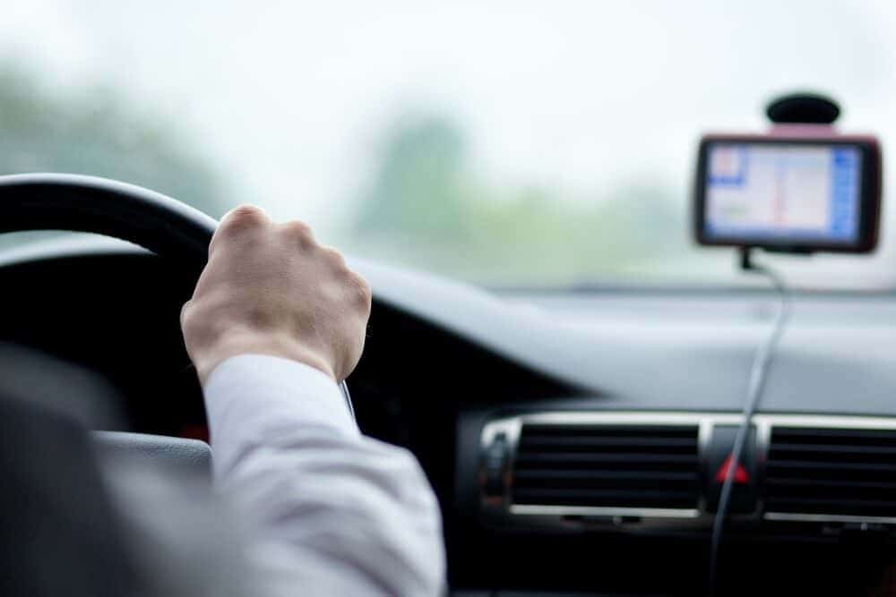 Driver's hand on steering wheel, GPS device mounted on car dashboard displaying navigation route.